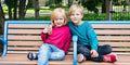 Two children sitting on a park bench, smiling while wearing their long sleeve Raspberry and Twilight RightSide Childrens sensory friendly and reversible shirts